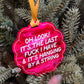 A bright pink scalloped Christmas ornament with white text hanging from a yellow ribbon on a green pine tree.