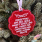 A red glitter Christmas ornament with white text reading 'POINSETTIAS ARE RED, JESUS WASN'T RED/WHITE, AND ALL I WANT FOR CHRISTMAS ARE BASIC HUMAN RIGHTS' hanging from a white ribbon on a green Christmas tree.