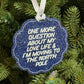 A scalloped blue glitter Christmas ornament with white text reading 'ONE MORE QUESTION ABOUT MY LOVE LIFE & I'M MOVING TO THE NORTH POLE', hanging from a white ribbon on a green pine tree.