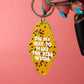 A hand with turquoise nail polish holds a yellow glitter keychain with black stars and the text 'ON MY WAY TO MAKE THE VIBE WEIRD' against a solid pink background.